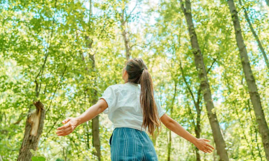 vrouw staat tussen bomen en ademt schone lucht in
